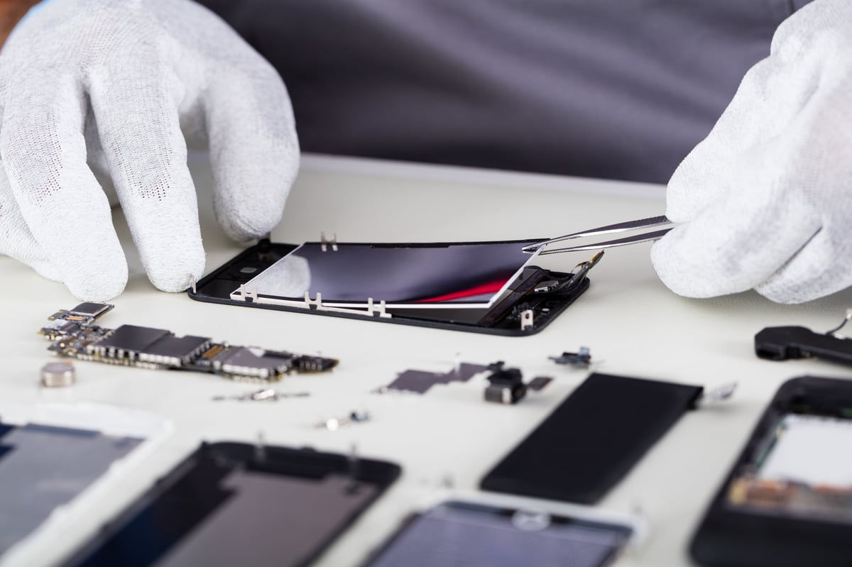 Technician working closely on a disassembled smartphone with tweezers